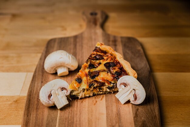 Un trozo de quiche con champiñones y queso sobre tabla de madera