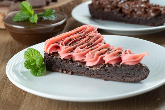 Trozo de rebanada de brownie de chocolate con glaseado de fresa y chocolate Mesa de madera con menta y chispas de chocolate en el fondo