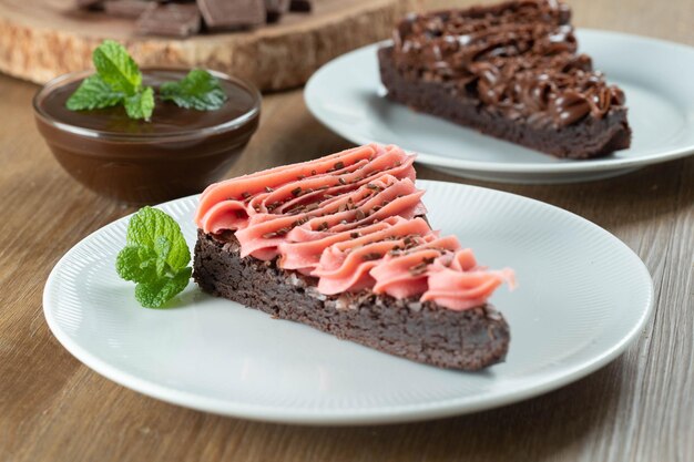 Trozo de rebanada de brownie de chocolate con glaseado de fresa y chocolate Mesa de madera con menta y chispas de chocolate en el fondo