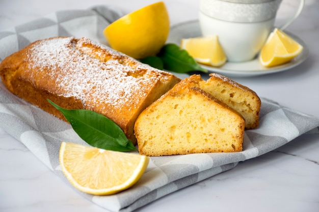 Trozo de tarta de limón sobre papel de cocina con limones y taza de té. Receta fácil de postre cítrico para cocinar todos los días.