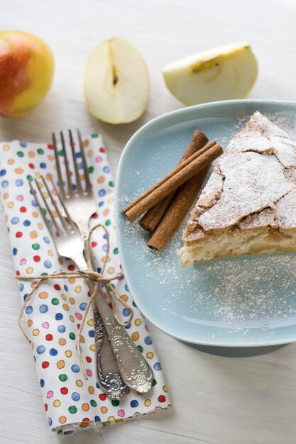 Un trozo de tarta de manzana sobre placa azul, manzana, canela, tenedores de un color