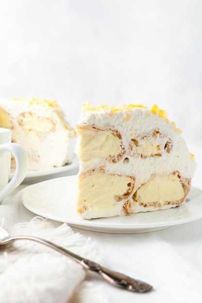 Un trozo de tarta de natillas con crema batida Decorado con chispas de chocolate amarillo Hecho en casa En un plato blanco Cerca de una cuchara y una taza Al fondo hay un plato con tarta y una tetera blanca