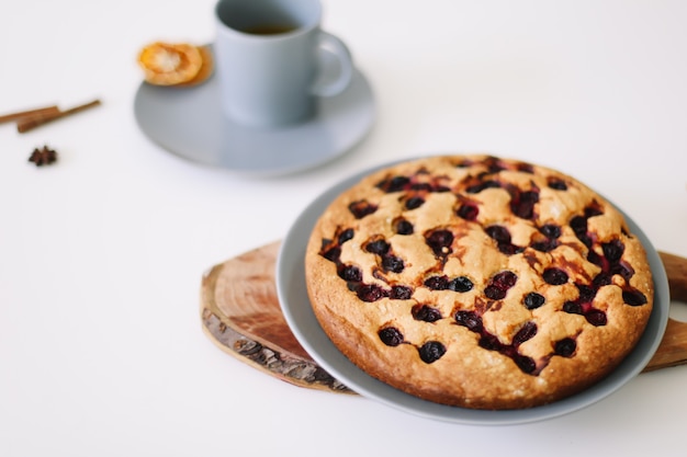 Trozo de tarta en un plato con una taza de té en el desayuno de mesa blanca