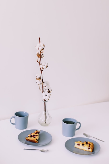 Trozo de tarta en un plato con una taza de té en el desayuno de mesa blanca