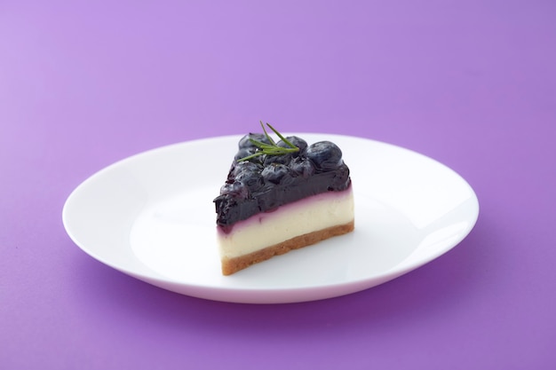 Trozo de tarta de queso de arándanos en la placa blanca sobre fondo violeta