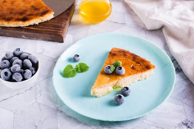 Un trozo de tarta de queso con miel y arándanos en un plato sobre la mesa