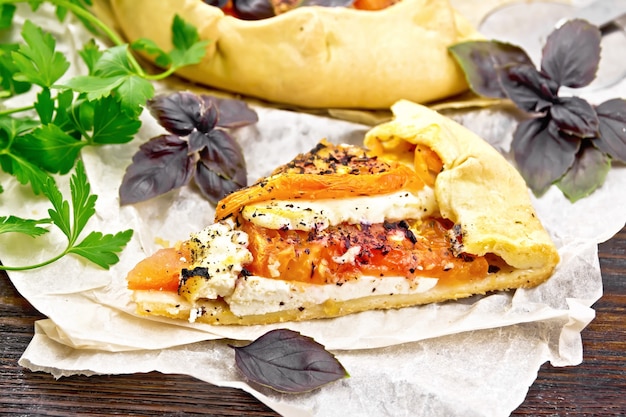 Trozo de tarta con tomates, requesón y albahaca morada sobre pergamino sobre fondo de placa de madera