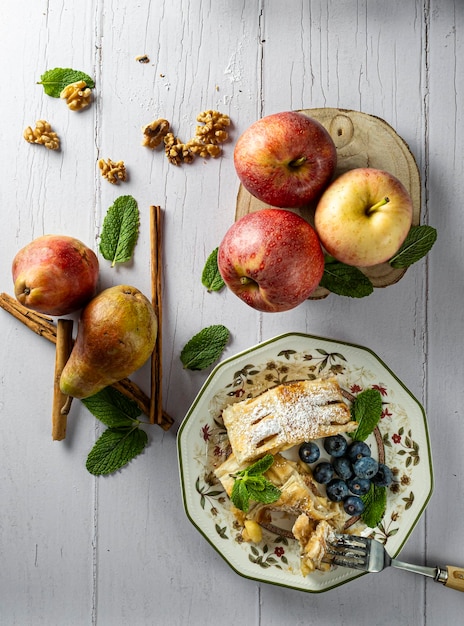 Un trozo tradicional de strudel de manzana con azúcar en polvo, menta, arándanos y canela en primer plano sobre una mesa