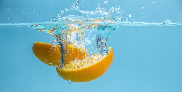 Trozos de apetitosa naranja madura caen al agua clara, formando muchas salpicaduras