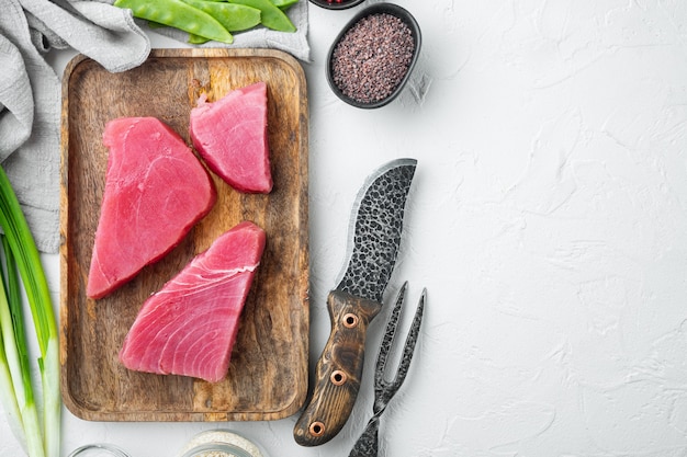 Trozos de atún crudo con ingredientes guisante verde, sésamo y hierbas, en bandeja de madera, en piedra blanca