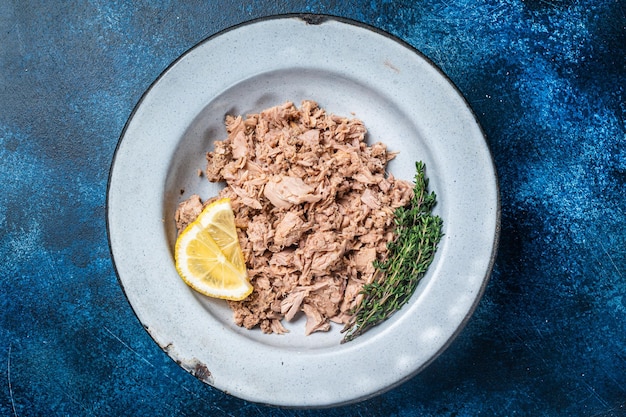 Trozos de atún enlatados en aceite de oliva listos para comer Fondo azul Vista superior