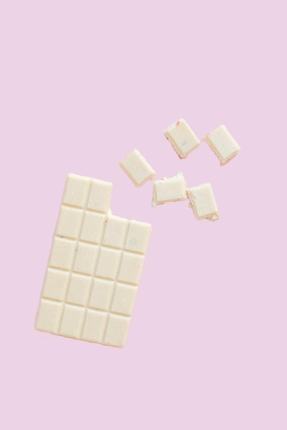 Trozos de una barra de chocolate blanco volando en el aire aislado sobre un fondo de color rosa