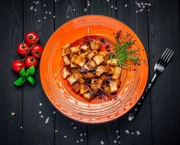 Trozos de berenjena frita en un plato de color sobre un fondo oscuro