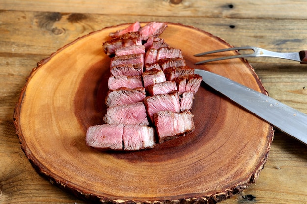 Trozos de bistec ancho cortados bajo una tabla de madera con tenedor y cuchillo al lado vista lateral