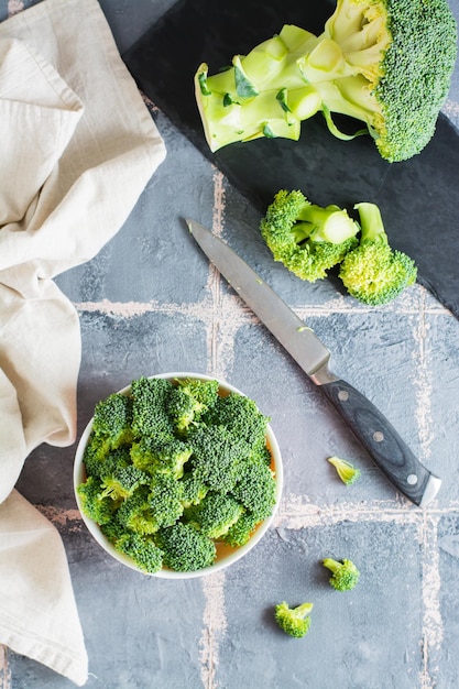Trozos de brócoli crudo en un tazón y un cuchillo sobre la mesa Cocinar comida vegetariana saludable Vista superior y vertical