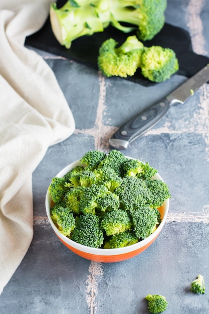 Trozos de brócoli crudo en un tazón y un cuchillo sobre la mesa Cocinar comida vegetariana saludable Vista vertical