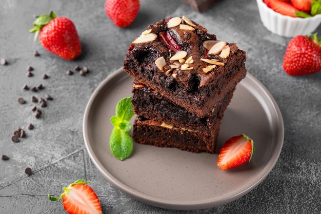 Trozos de brownie de chocolate con nueces, fresa y helado en un plato sobre un fondo oscuro