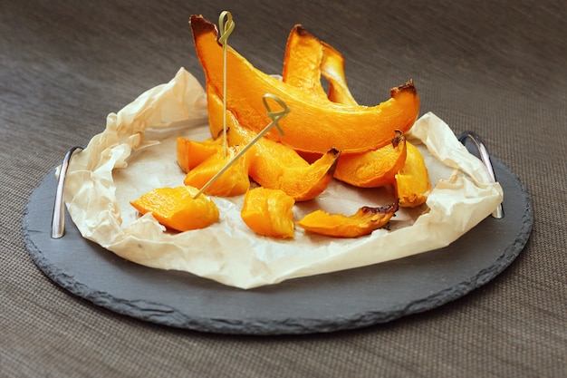 Trozos de calabaza al horno en almíbar de azúcar sobre papel y bandeja negra.