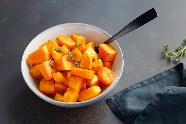 Trozos de calabaza asada con tomillo fresco en un cuenco de cerámica sobre una mesa Receta de temporada de otoño