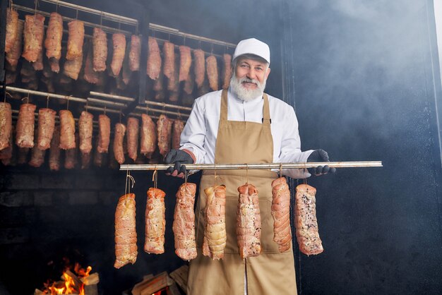 Trozos de carne ahumada y carnicero posando en ahumadero.