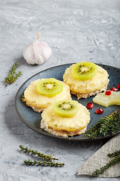 Trozos de carne de cerdo al horno con piña, queso y kiwi sobre fondo gris.