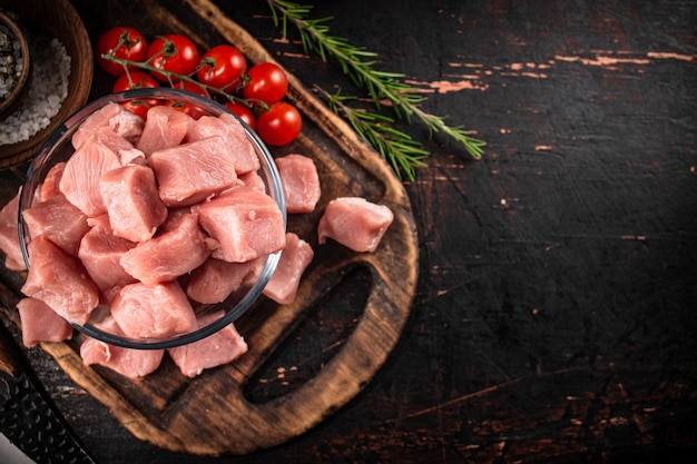 Foto trozos de carne de cerdo cruda en un recipiente de vidrio con tomates y romero