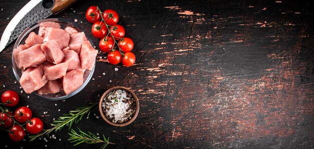 Trozos de carne de cerdo cruda en un recipiente de vidrio con tomates y romero