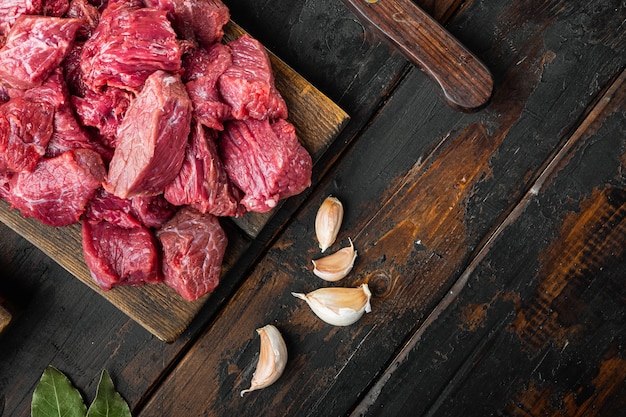 Trozos de carne fresca servidos en la mesa con ingredientes listos para cocinar, en la vieja mesa de madera oscura, vista superior plana