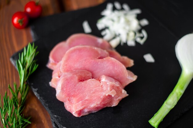 Trozos de carne de pavo cruda en rodajas, cebollas picadas, sobre un fondo de pizarra negra.