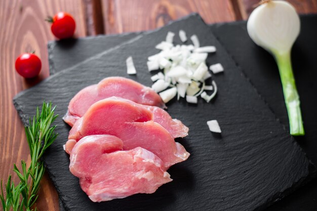 Trozos de carne de pavo cruda en rodajas, cebollas picadas, sobre un fondo de pizarra negra.