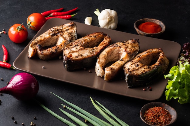 Trozos de carpa a la plancha en un plato con tomites pimientos cebollas rojas ajo