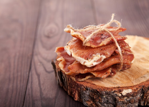 Trozos de cecina en un montón atados con un cordel yacen sobre un corte de un árbol sobre un fondo de madera. Copia spaes.