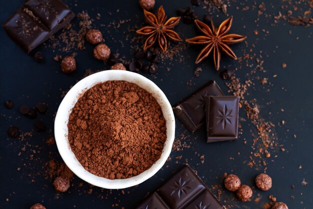 Trozos de chocolate, cacao en polvo y especias en la mesa de pizarra oscura, vista superior de ingredientes de cocina