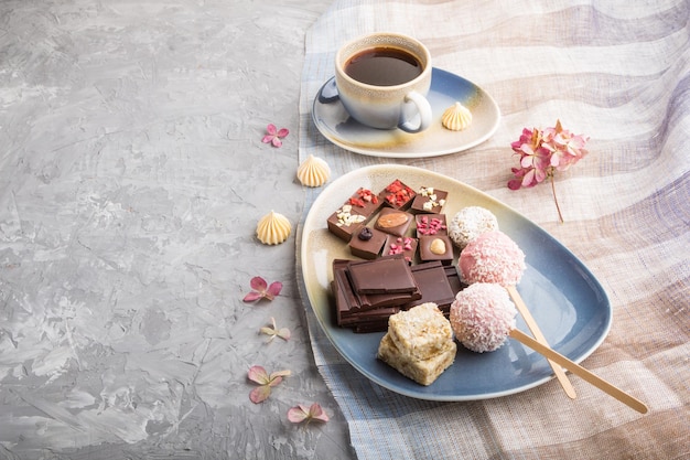 Trozos de chocolate casero con dulces de coco y una taza de café en un espacio de copia de vista lateral de fondo de hormigón gris