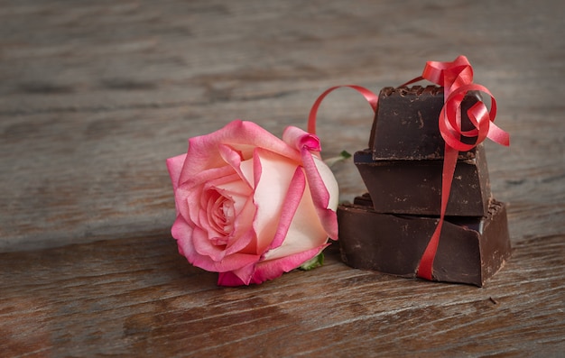 Trozos de chocolate y flor en el fondo de madera. Tres piezas de chocolate con cinta roja y rosa sobre superficie de madera oscura.