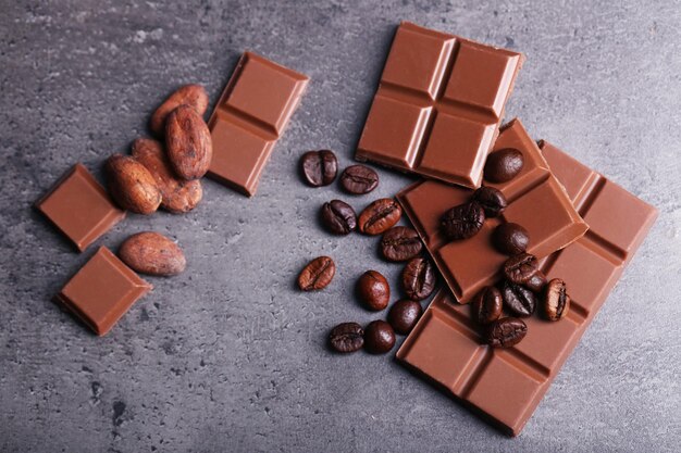 Trozos de chocolate con leche y granos de café sobre fondo gris