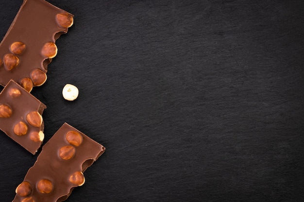 Trozos de chocolate con leche con nueces sobre un fondo oscuro. Vista superior con espacio de copia.