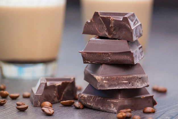 Trozos de chocolate negro, granos de café y tazas de cacao o café con leche en la mesa de madera.