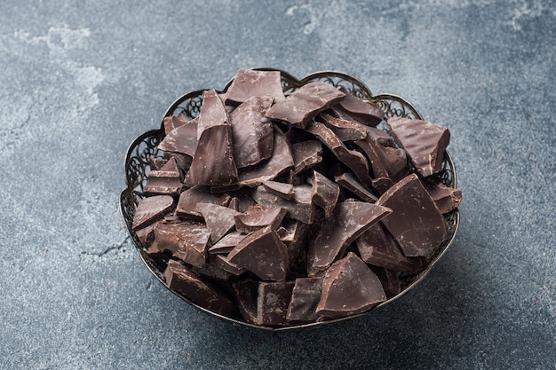 Trozos de chocolate negro triturado en un plato en un oscuro.