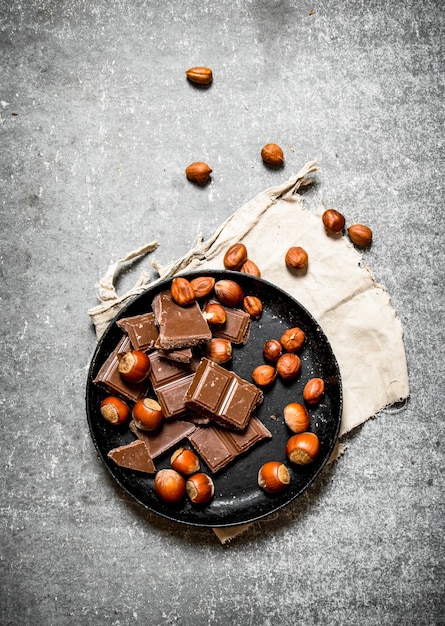 Trozos de chocolate con nueces en el plato antiguo. Sobre la mesa de madera negra.