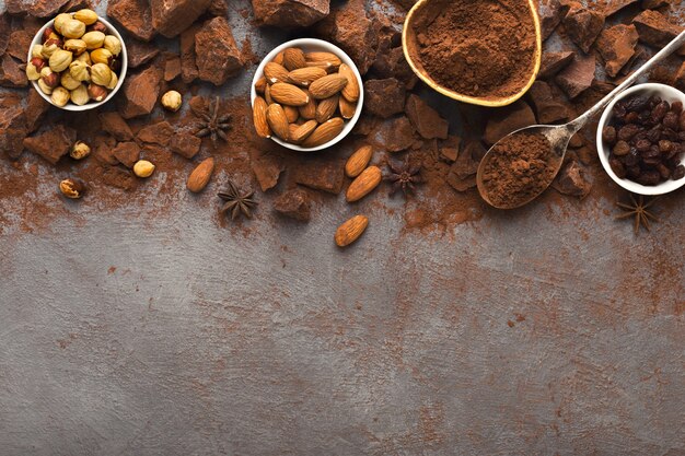 Trozos de chocolate roto oscuro sobre fondo oscuro, cacao en polvo y varios frutos secos en tazones de fuente. Papel tapiz dulce, concepto de ingredientes de cocina y publicidad de confitería, vista superior, espacio de copia