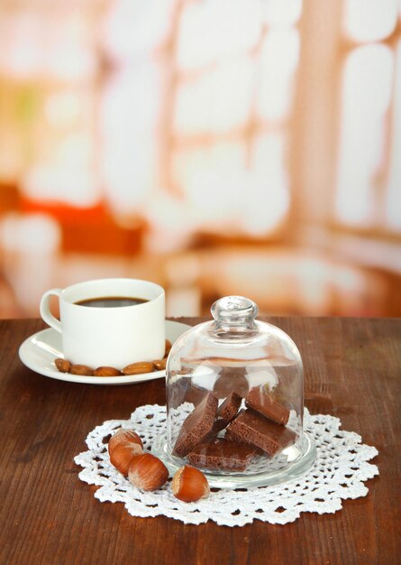 Trozos de chocolate bajo la tapa de vidrio y bebida caliente sobre fondo brillante