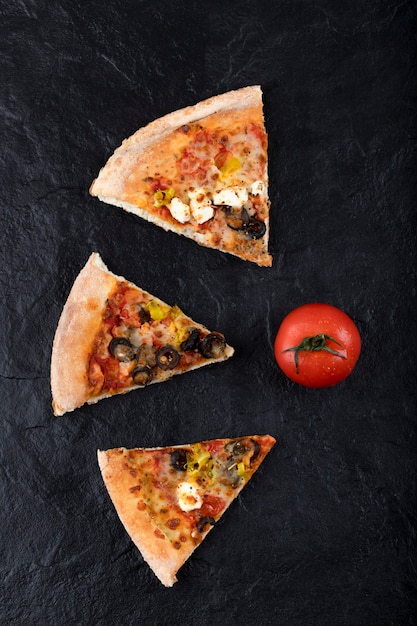 Trozos de deliciosa pizza con tomate rojo fresco colocado sobre un fondo negro.