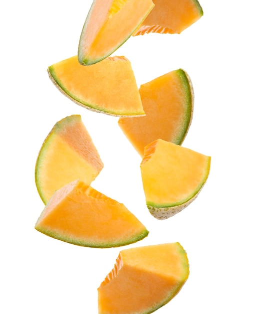 Trozos de delicioso melón maduro cayendo sobre fondo blanco.