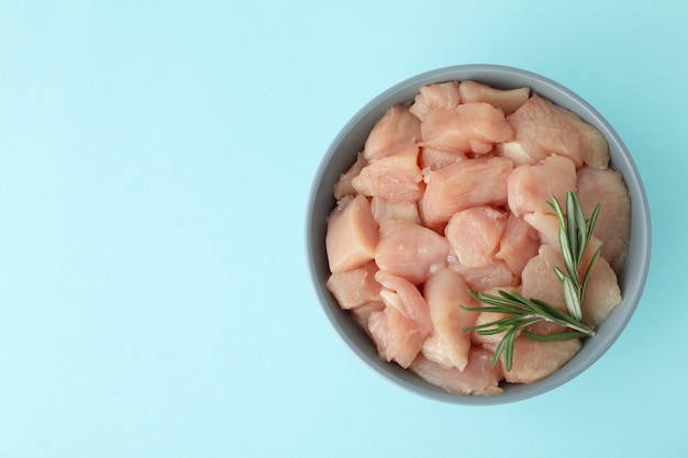 Trozos de filete de pollo crudo en un tazón sobre fondo azul.