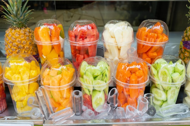 Trozos de frutas exóticas en vasos de plástico para bebidas de jugo en hielo en el puesto del mercado. Refresco saludable