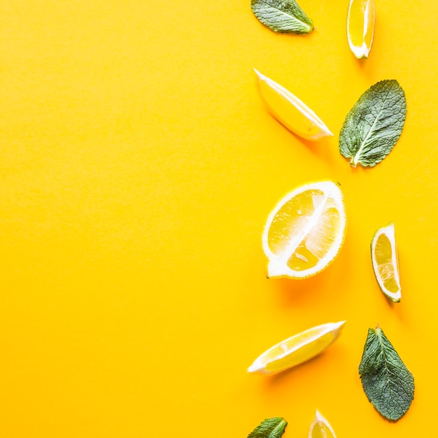 Trozos de limón, lima y hojas de menta verde sobre un fondo amarillo