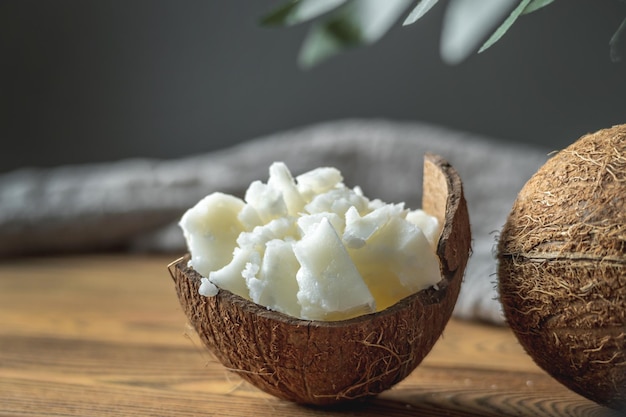 Trozos de mantequilla de coco orgánica en un bol y coco fresco en una mesa de madera Concepto de ingrediente saludable para cocinar y cosmética natural