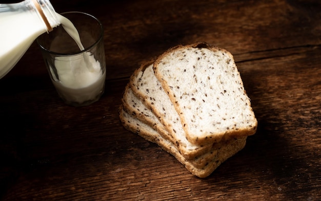 Trozos de pan con semillas y leche se vierten en un vaso Fondo de madera oscura Desayuno matutino Comida saludable