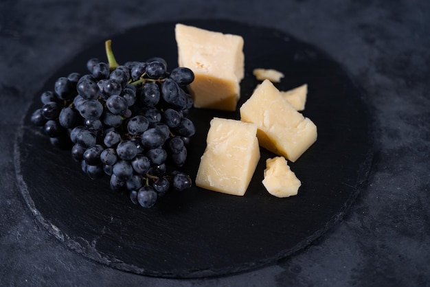 Foto trozos de parmesano aromático y uvas pasas negras sobre un fondo oscuro. plato de vino.